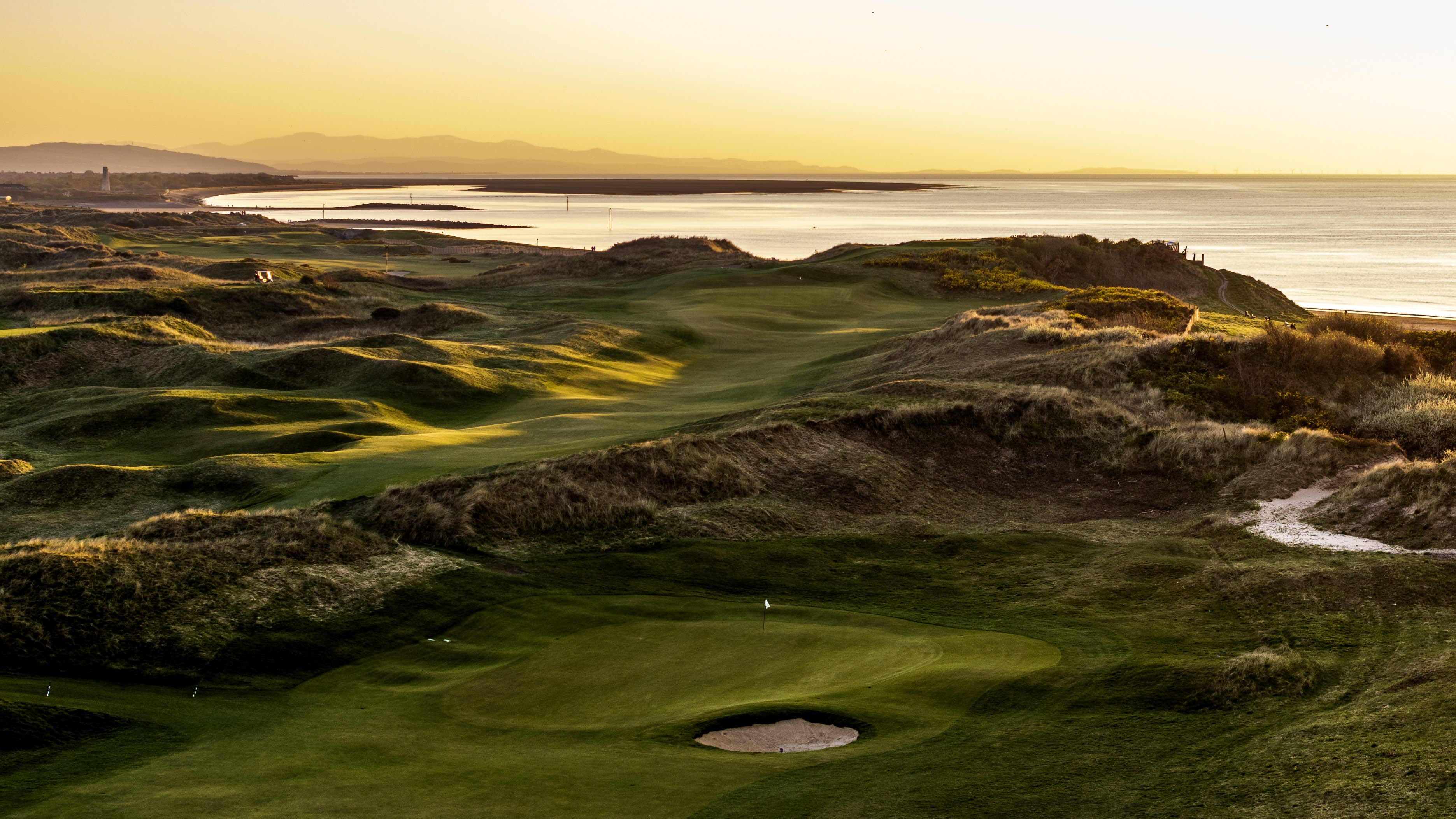 A green and its bunker in the dunes at sunset, the estuary and the hills beyond