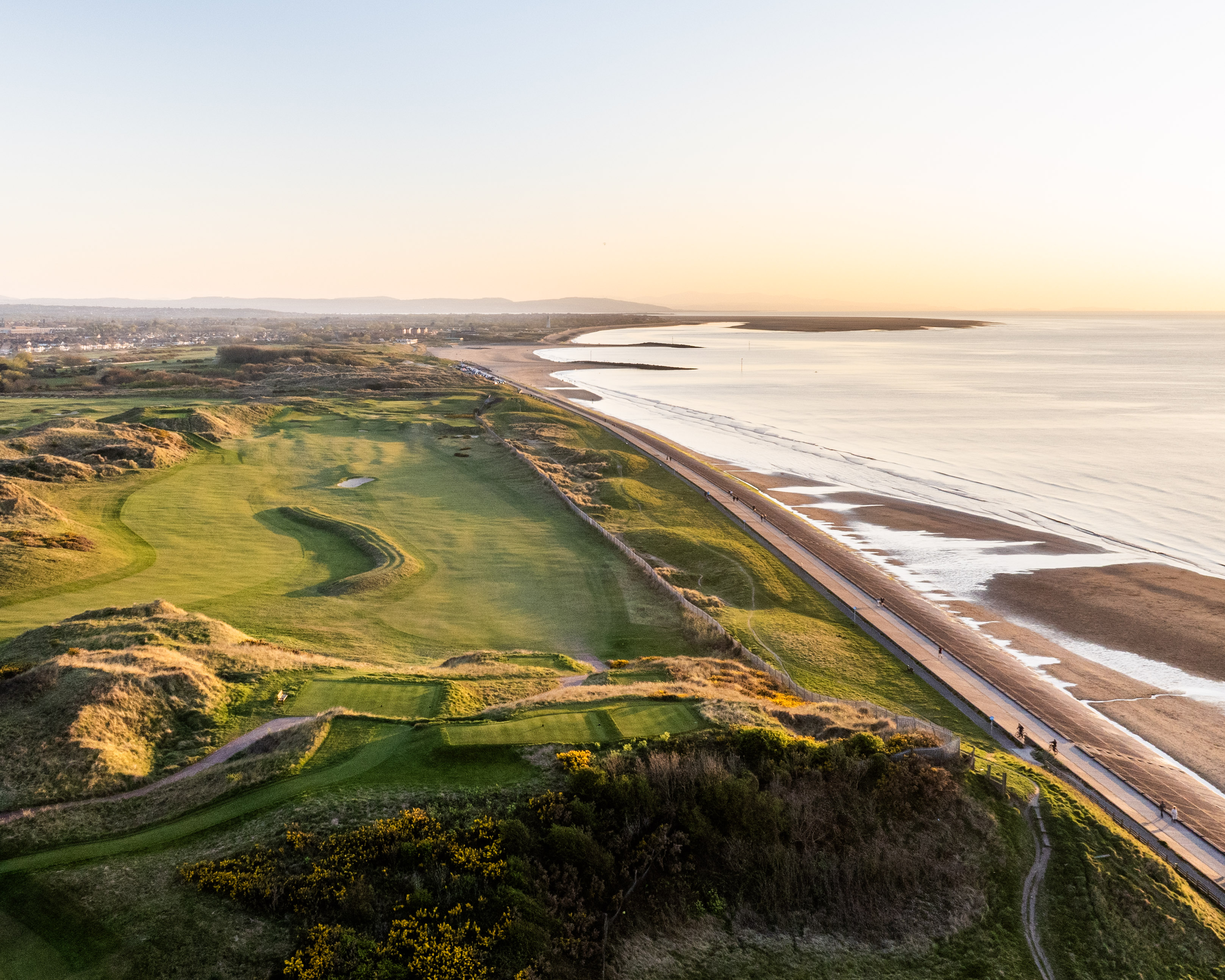 The links beside the promenade and beach from the air, the coast curving away to the hills