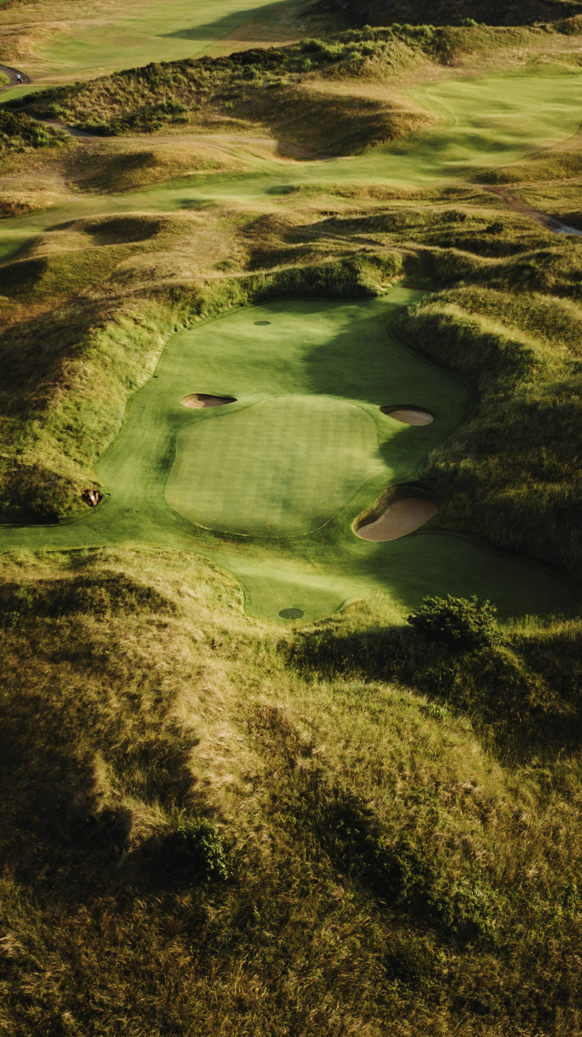 The short game green from higher overhead, framed by the surrounding dunes